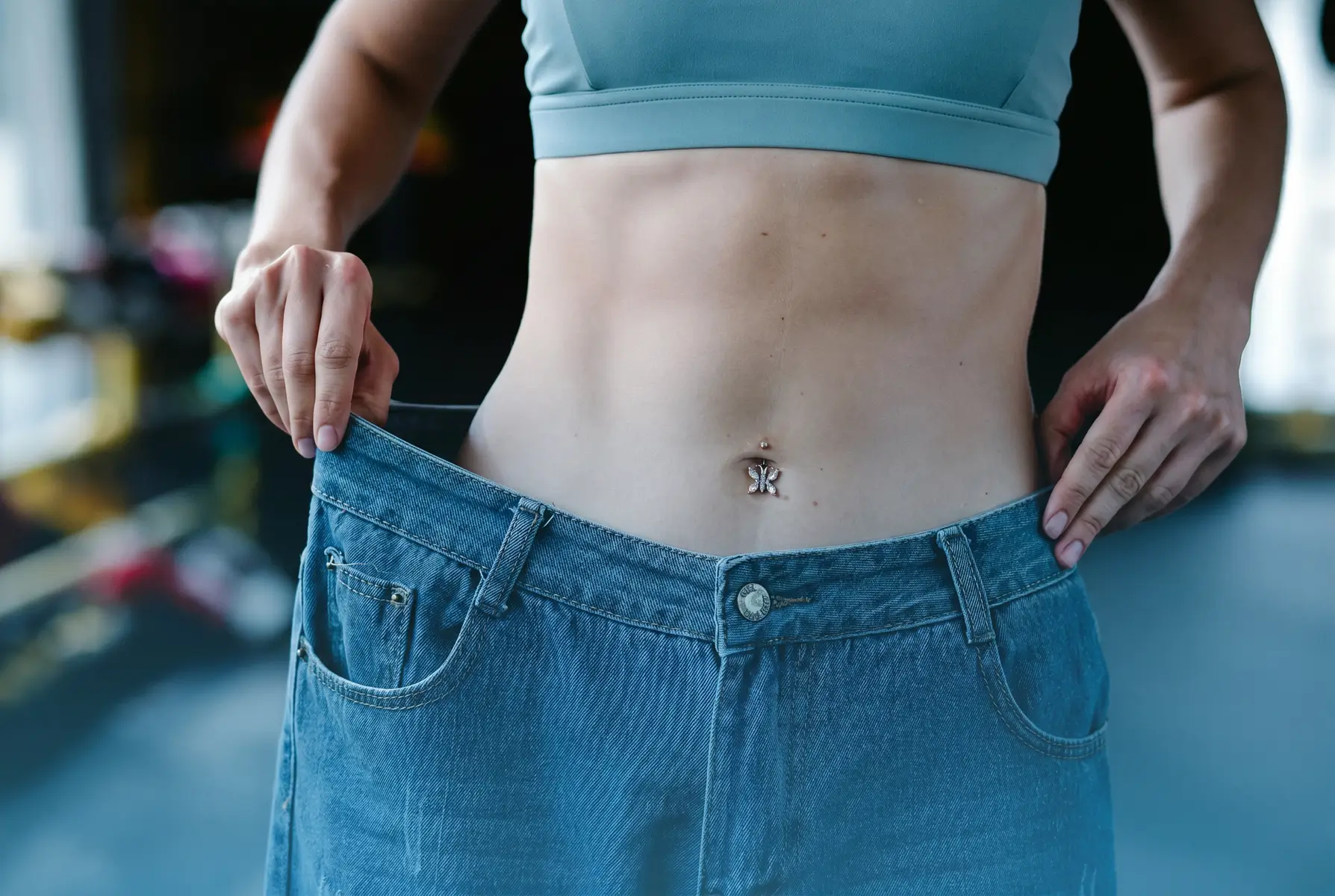 Woman showing weight loss results in oversized jeans after testosterone therapy for women
